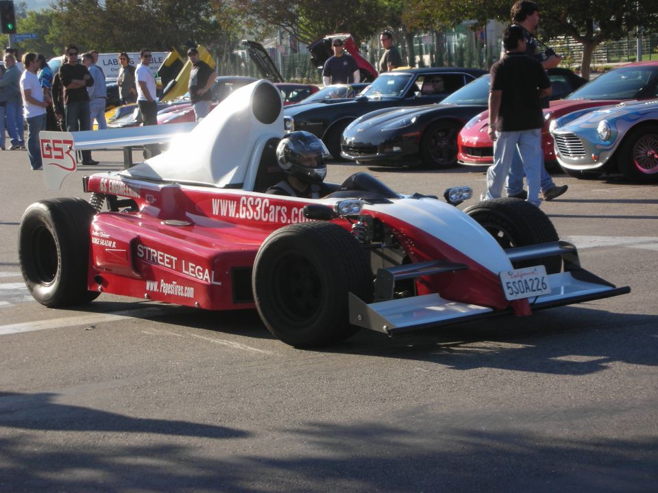 Red and white open-wheel formula-style race car driven in a lot
