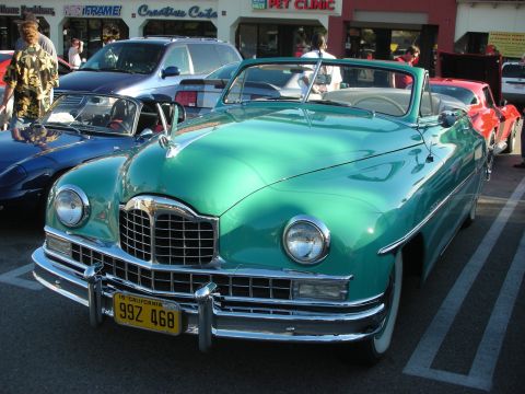 1998 Ford Crown Victoria - teal-green late-1940s convertible with a heavy chrome grille and a 1949 California license plate, displayed at an outdoor car show.