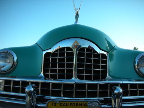 1998 Ford Crown Victoria - Close-up front view of a teal-green vintage car showing its waterfall chrome grille, dual headlights and winged hood ornament.