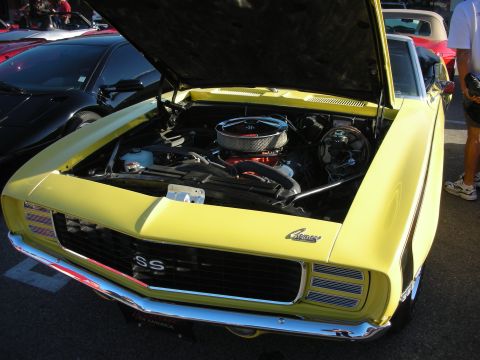 1998 Ford Crown Victoria - yellow Chevrolet Camaro SS with its hood raised, revealing a chrome-topped V8 engine, at an outdoor car meet.