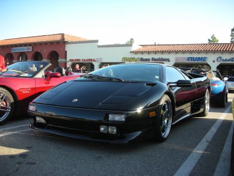 1998 Ford Crown Victoria - black Lamborghini Diablo with black alloy wheels parked at a curbside car gathering in front of shops.