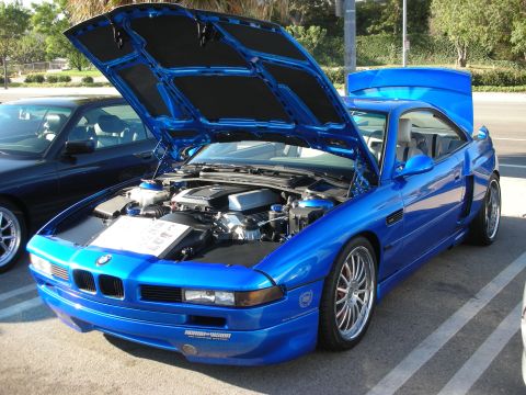 1998 Ford Crown Victoria - blue BMW 8 Series coupe with hood raised, displaying its V8 engine bay above an open photo binder.