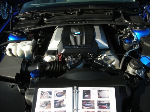 1998 Ford Crown Victoria - Detailed view of a BMW V8 engine bay with blue-capped fluid reservoirs and an open photo album resting on the front edge.