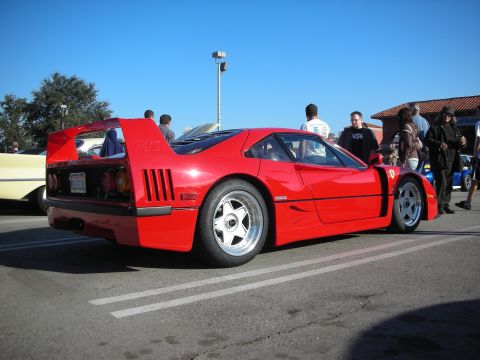 1998 Ford Crown Victoria - red Ferrari F40 with its large rear wing and five-spool wheels, parked among spectators at an outdoor car show.