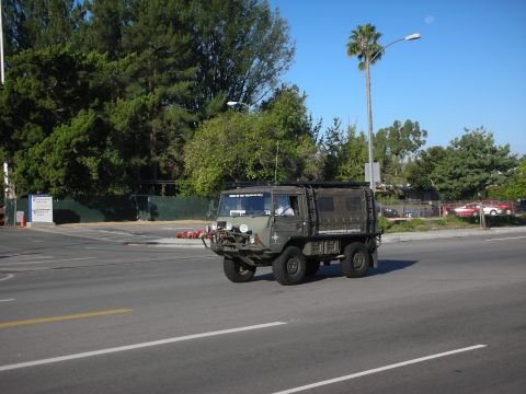 1998 Ford Crown Victoria - small olive-drab military-style 4x4 truck with a winch and canvas-topped bed crossing a roadway lined with trees.