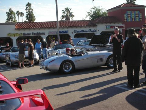 1998 Ford Crown Victoria - silver custom open-top roadster with wire-spoke wheels parked at a busy car gathering as spectators look on.