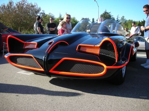 1998 Ford Crown Victoria - Low front view of a black 1960s-style Batmobile replica with bright orange-red edge trim and twin clear bubble canopies.