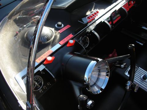 1998 Ford Crown Victoria - Close-up of a Batmobile replica's black dashboard with chrome trim, a domed gauge and red-labeled control switches.