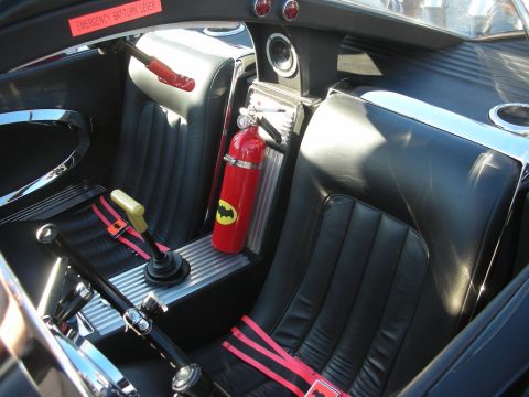 1998 Ford Crown Victoria - Interior of a black Batmobile replica showing black bucket seats and a red fire extinguisher marked with a bat emblem.