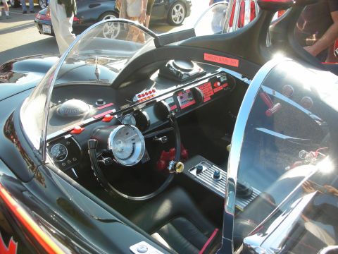 1998 Ford Crown Victoria - View into a black Batmobile replica cockpit showing the steering wheel, center console and red-labeled dashboard switches.