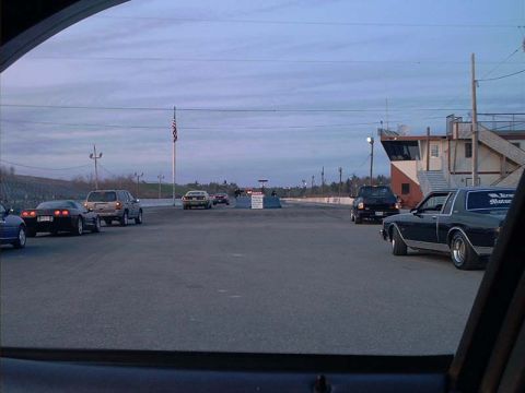 2000 Ford Crown Victoria - Cars are staged on the asphalt at a drag strip, with a building and flag visible in the distance.