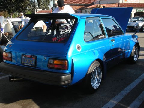 1998 Ford Crown Victoria - modified blue hatchback with flared fenders, racing decals, and a California plate reading LESKO83 parked at a car meet.