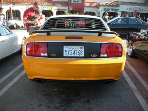 1998 Ford Crown Victoria - Straight-on rear of an orange-yellow Ford Mustang with rear window louvers, spoiler, and California plate 5YSW768 at a strip mall.