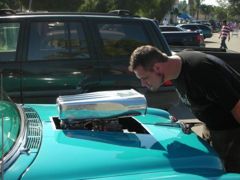1998 Ford Crown Victoria - A man inspects a turquoise hot rod a prominent chrome blower protruding from its hood, with an SUV visible in the background.