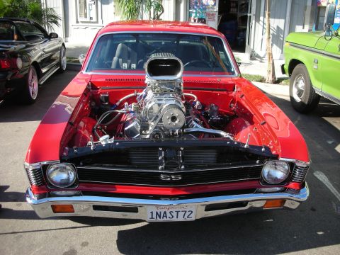 1998 Ford Crown Victoria - Custom red muscle car with a prominent supercharger, parked next to a green truck.