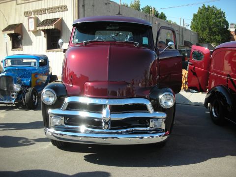 1998 Ford Crown Victoria - Maroon 1950s Chevrolet truck parked next to a blue hot rod at a show.