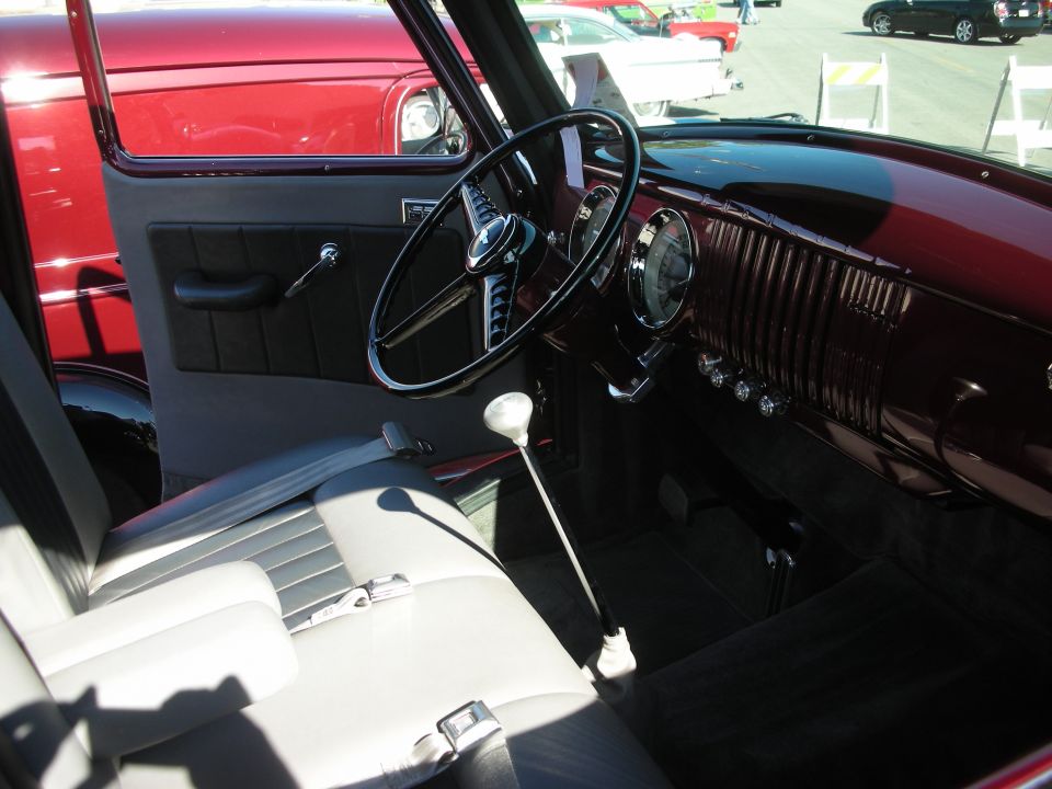 Interior of a vintage pickup truck with white bench seat, black steering wheel, floor shifter and dark red dash