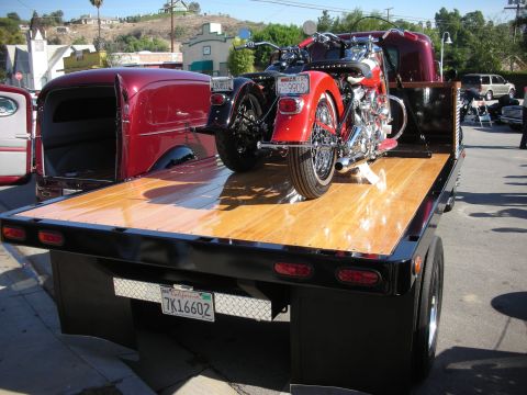 1998 Ford Crown Victoria - A red motorcycle is transported on a flatbed truck a polished wooden deck and a red classic truck bed.