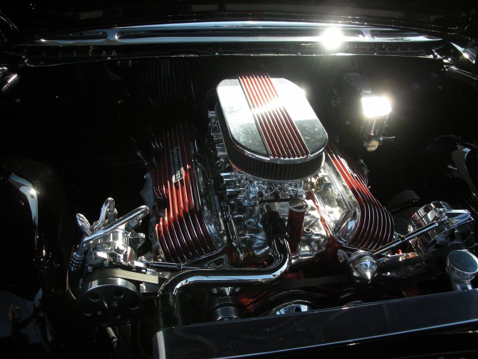 Chrome and red V8 engine with finned valve covers and oval air cleaner in a dark engine bay