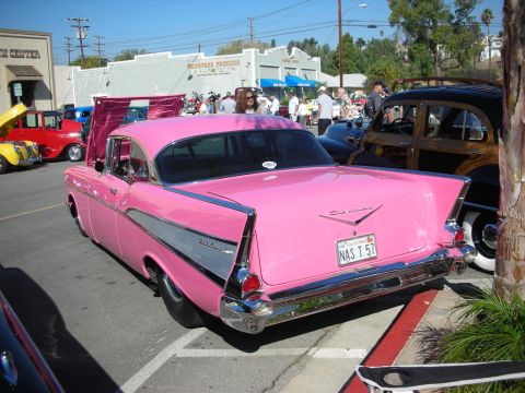 1998 Ford Crown Victoria - A pink 1957 Chevrolet Bel Air is parked at an outdoor car show with other vehicles visible.