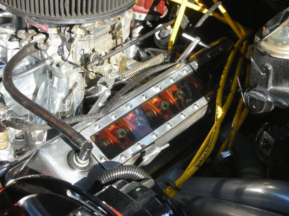 Close-up of a V8 engine bay showing a carburetor, valve cover and yellow spark plug wires