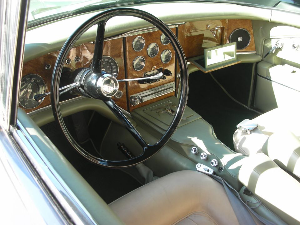Interior of a classic luxury coupe with black steering wheel, wood dash, round gauges and tan leather seats