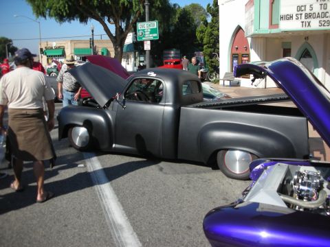 1998 Ford Crown Victoria - A customized matte black pickup truck is displayed at an outdoor event, with a purple custom car in the foreground.