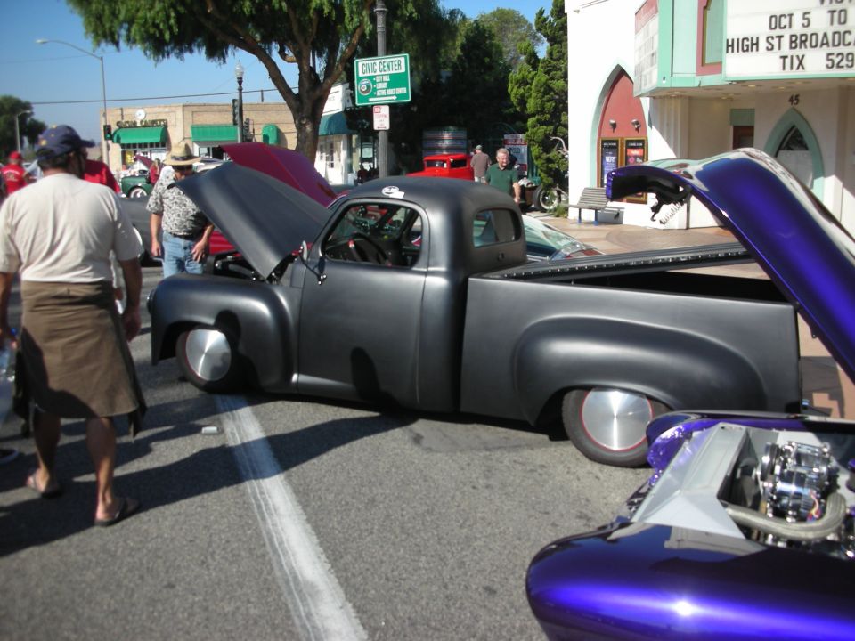 Gray custom pickup truck with hood up parked on a street at a car show near High Street theater