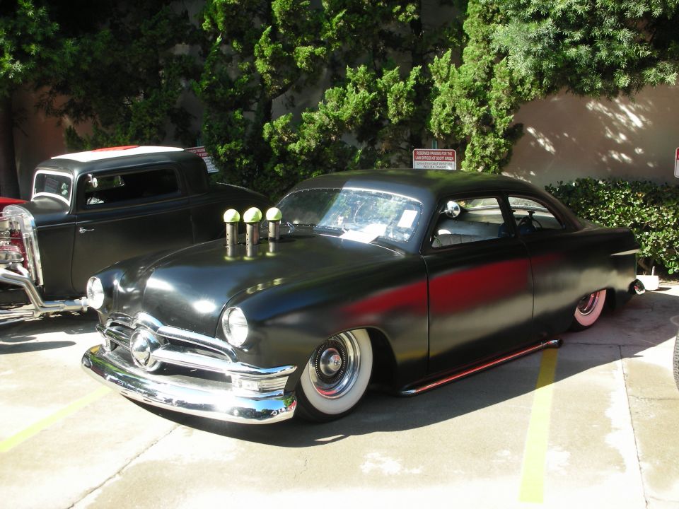 Black lowered custom coupe with three velocity stacks on the hood and whitewall tires parked outdoors