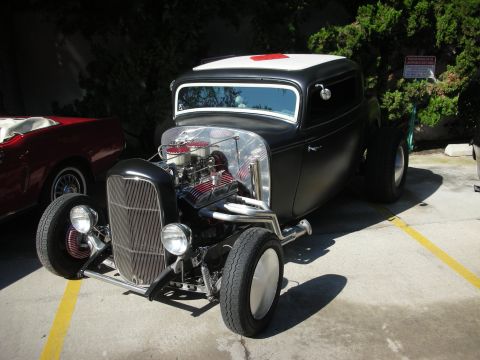 1998 Ford Crown Victoria - A custom hot rod with a prominent engine sits parked, with another vehicle visible to its left.