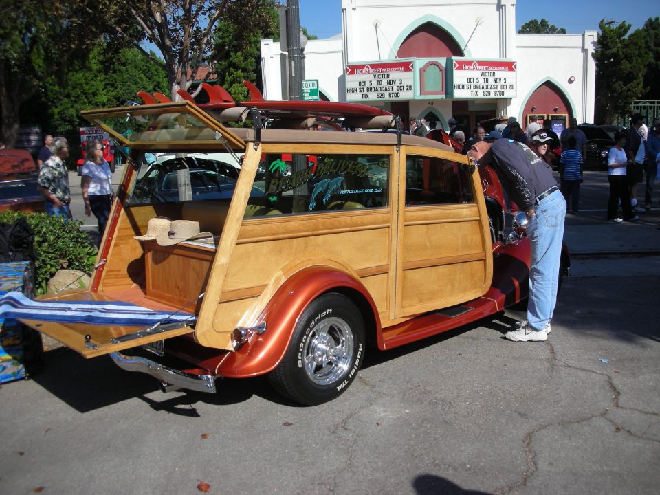 Orange and wood-paneled woodie station wagon hot rod parked outside a theater