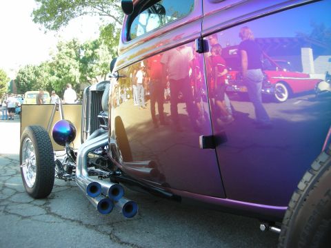 1998 Ford Crown Victoria - A custom hot rod with a striking purple paint job and prominent quad exhaust pipes is seen at an outdoor event, reflecting onlookers and an…