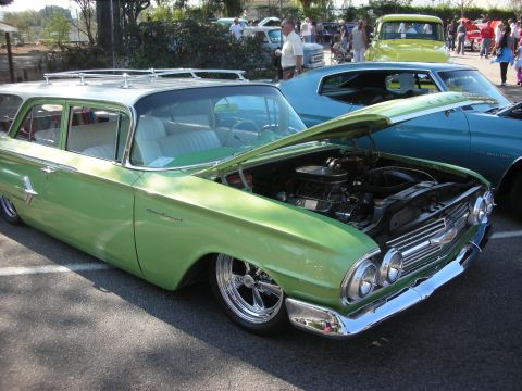 1998 Ford Crown Victoria - A green 1960 Chevrolet Brookwood station wagon is displayed with its hood open, alongside other vehicles at an outdoor event.