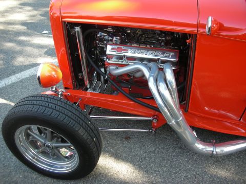 1998 Ford Crown Victoria - Exposed Chevrolet engine with chrome headers and valve covers on a bright red hot rod.