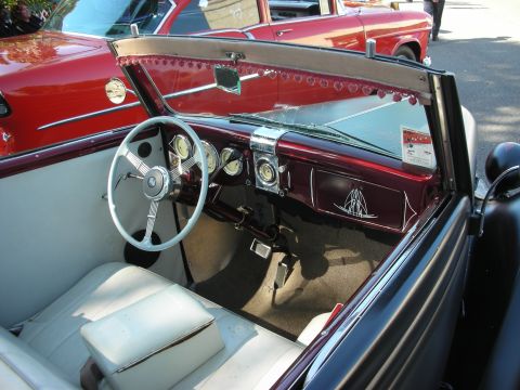 1998 Ford Crown Victoria - The dashboard of a vintage convertible features a large steering wheel and several gauges, with a red car parked alongside.