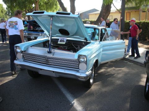 1998 Ford Crown Victoria - A light blue classic car is displayed with its hood open, attracting attention from onlookers at an outdoor event.