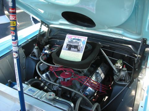 1998 Ford Crown Victoria - The engine bay of a classic car is shown, with a card displaying a vintage vehicle performing a wheelie.