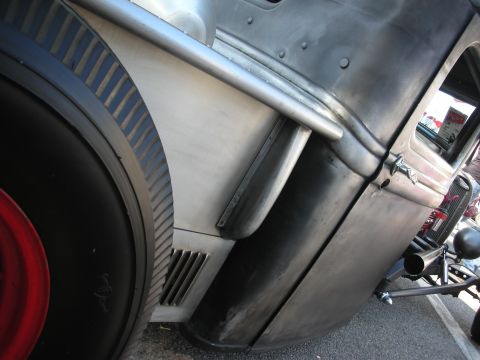 1998 Ford Crown Victoria - A custom hot rod displays its raw metal construction and large rear tire, with a glimpse of a fire extinguisher inside.