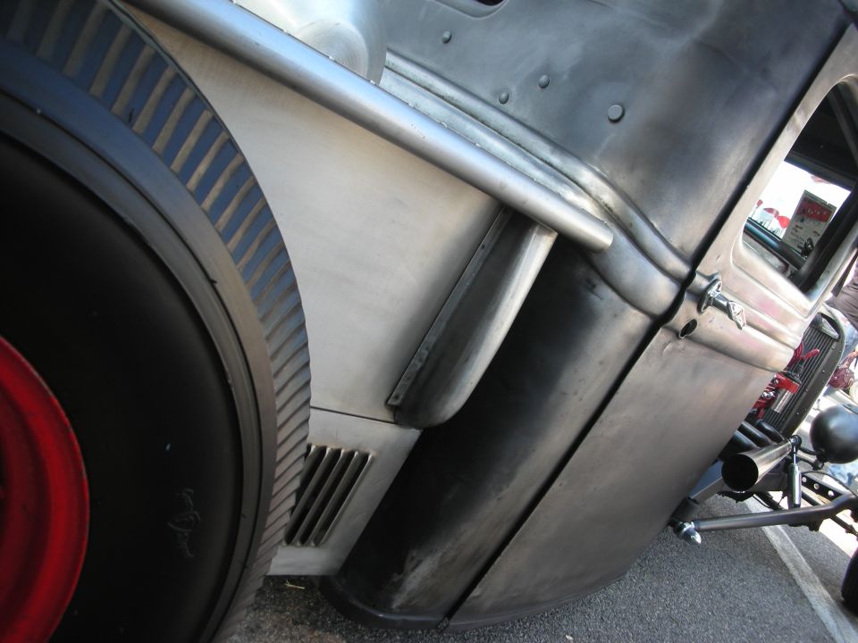 Bare-metal rat rod rear fender, wheel and exhaust detail close-up