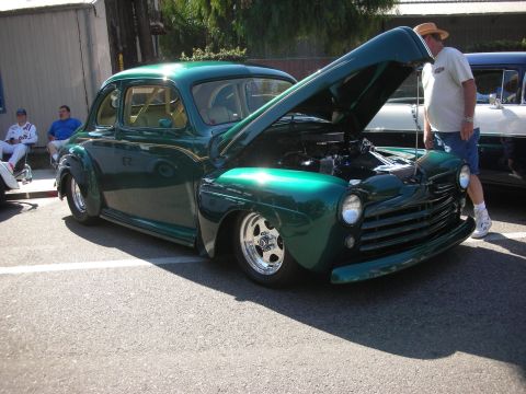 1998 Ford Crown Victoria - A man inspects the engine of a vintage green coupe at an outdoor car show.