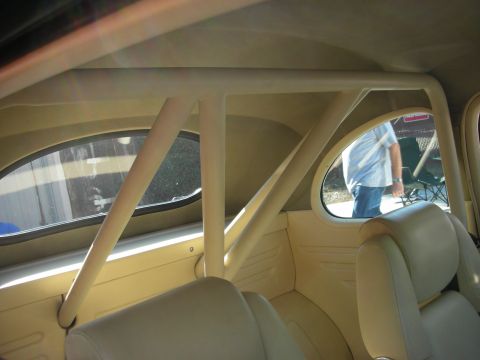 1998 Ford Crown Victoria - The interior of a car is shown, a prominent roll cage and tan leather seats, with a person visible through the rear window.
