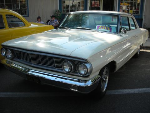 1998 Ford Crown Victoria - A white 1963 Ford Galaxie sedan is parked next to a yellow car, with a 'For Sale' sign in the window.