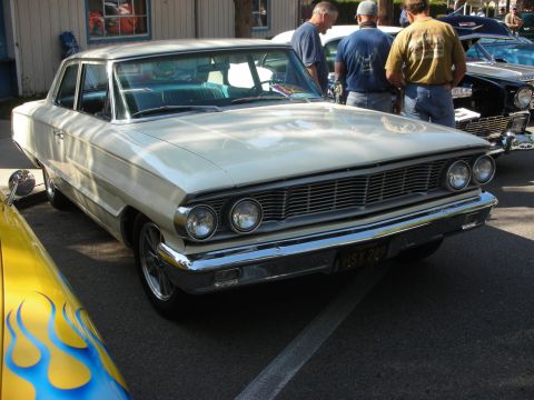1998 Ford Crown Victoria - A white 1963 sedan is parked at a show, with a yellow car with flames visible in the foreground.