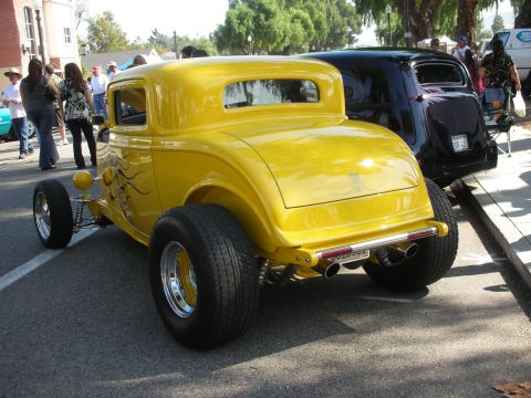 1998 Ford Crown Victoria - A yellow hot rod is parked next to a black car on a sunny day.