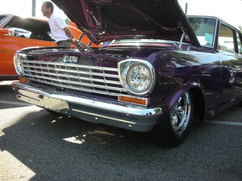 1998 Ford Crown Victoria - A man looks at the engine of a purple classic car parked at an outdoor event.
