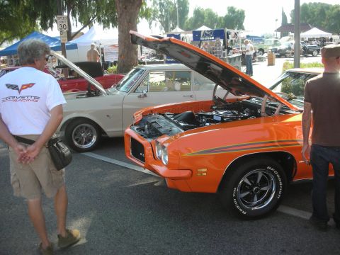 1998 Ford Crown Victoria - An orange muscle car is displayed with its hood open at an outdoor car show.