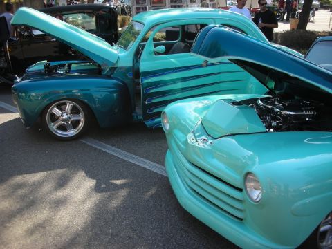 1998 Ford Crown Victoria - Two custom hot rod cars are parked side-by-side with their hoods open at an outdoor event.
