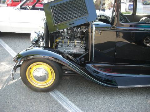 1998 Ford Crown Victoria - Front fender and engine bay of a black hot rod, with a white car visible behind it.