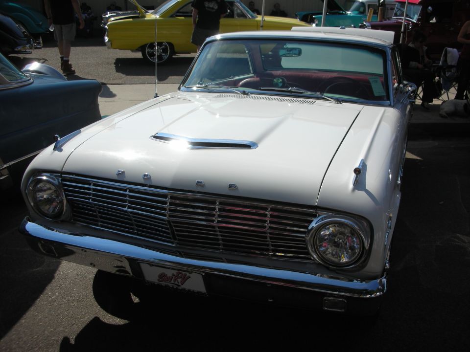 White Ford compact car front view with FORD lettered grille and hood scoop at car show
