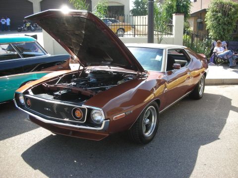 1998 Ford Crown Victoria - A brown AMC Javelin is displayed with its hood open, parked alongside another classic car.